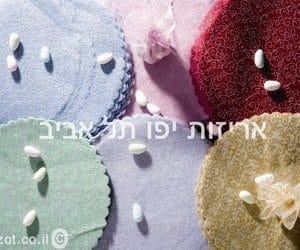 products-IMG_7706-copy חתיכות עגולות וצבעוניות עשויות טולי מבד אורגנזה - מנצנץ עם קצוות מסולסלים מסודרות על משטח, וכל אחת מהן מעוטרת בסוכריות לבנות. טקסט בעברית וכתובת Arizot.co.il מופיעים על גבי התמונה.