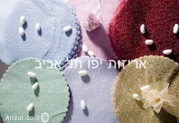 products-IMG_7706-copy חתיכות עגולות וצבעוניות עשויות טולי מבד אורגנזה - מנצנץ עם קצוות מסולסלים מסודרות על משטח, וכל אחת מהן מעוטרת בסוכריות לבנות. טקסט בעברית וכתובת Arizot.co.il מופיעים על גבי התמונה.