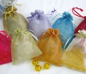 products-resample שקיות אורגנזה חלקות צבעוניות עם סרט קשירה מוצגות על משטח לבן; בחלקן מטבעות זהב, וחלק מהמטבעות מונחים גם לפני השקיות.